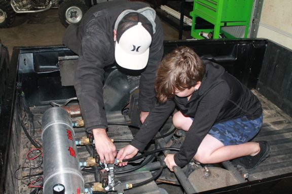 Father and son work on air hydraulics in the bed of a pickup